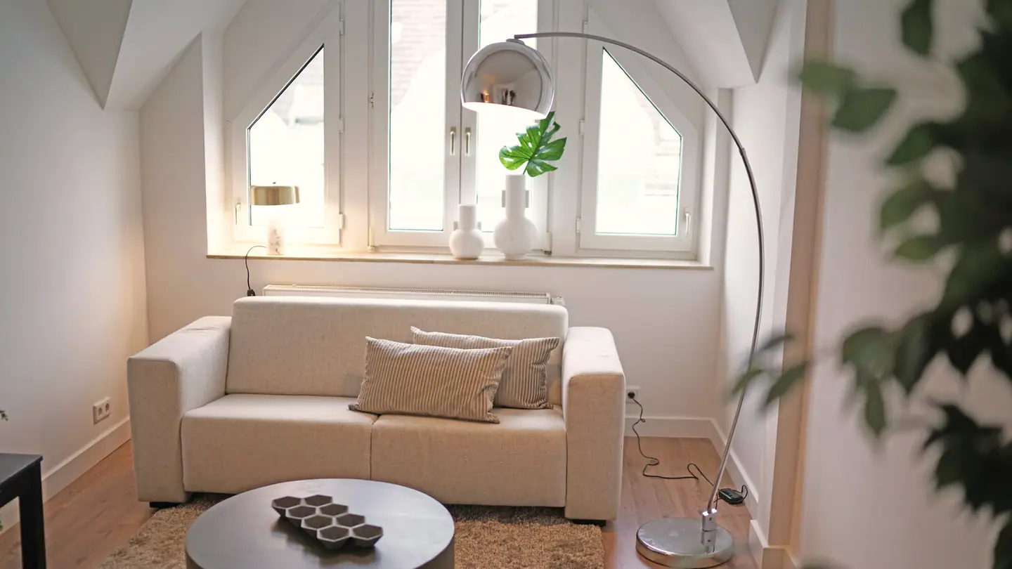 Wohnraum unter dem Dach mit Giebelfenster, Sofa und Bogenlampe